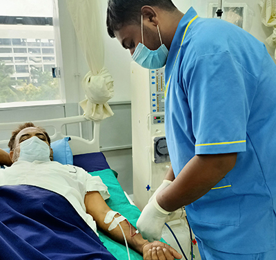 A patient is in a hospital bed, and a staff nurse is administering an injection to him.