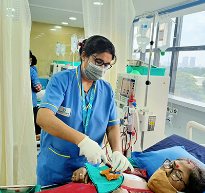 A woman in a hospital bed and a nurse administering an injection to her.